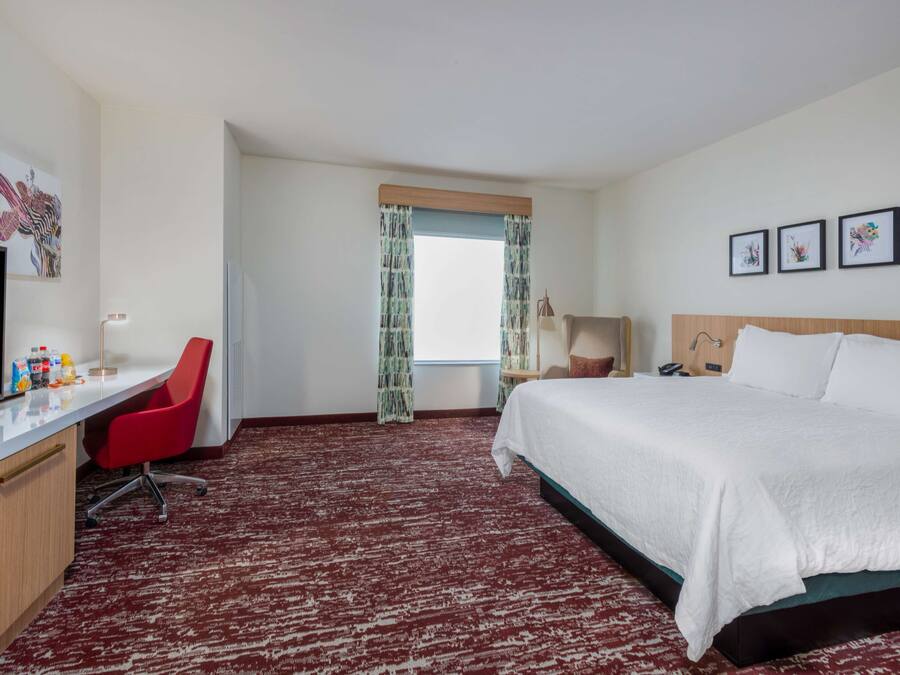 A hotel room with a bed, desk, chair, television, and artwork on the walls.