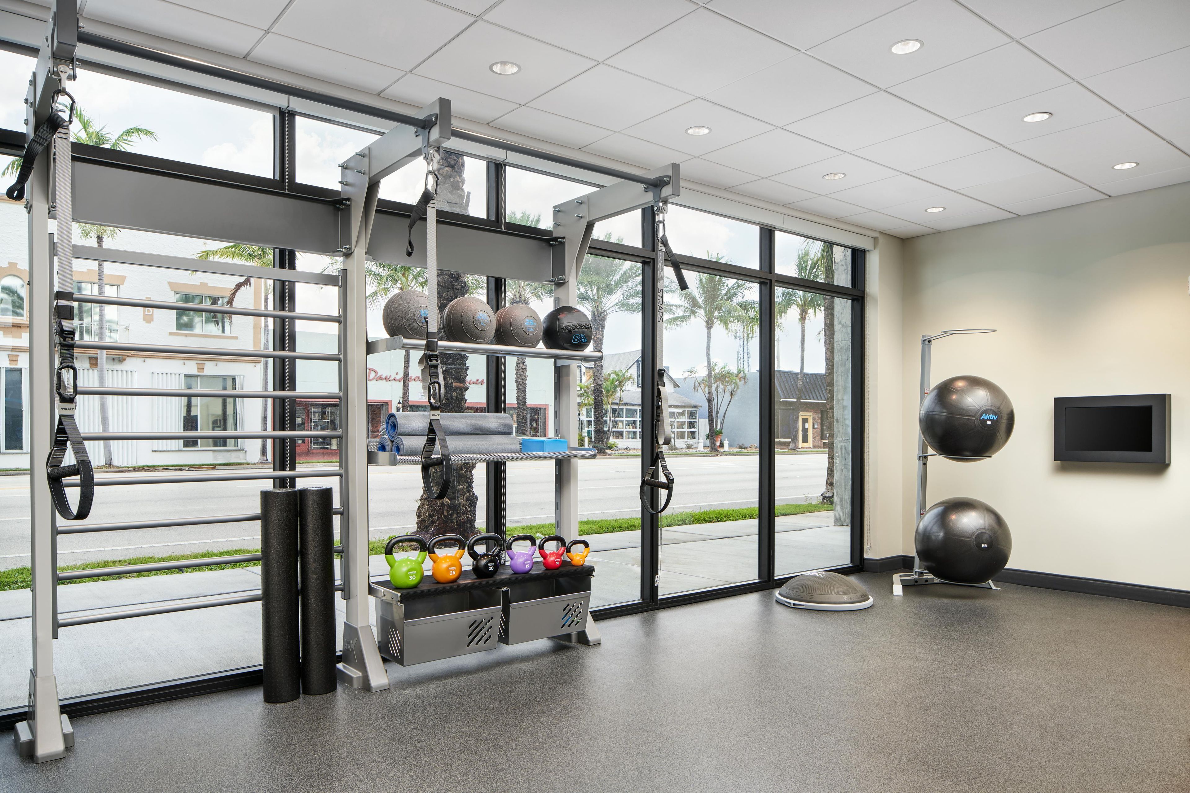 Un gimnasio con equipamiento de ejercicio, ventanas amplias y vistas al exterior.