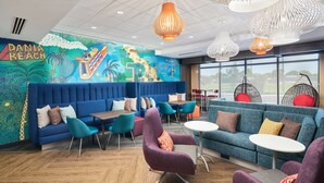 A modern lounge area with a mural of a beach, blue sofas, teal chairs, and unique pendant lights.