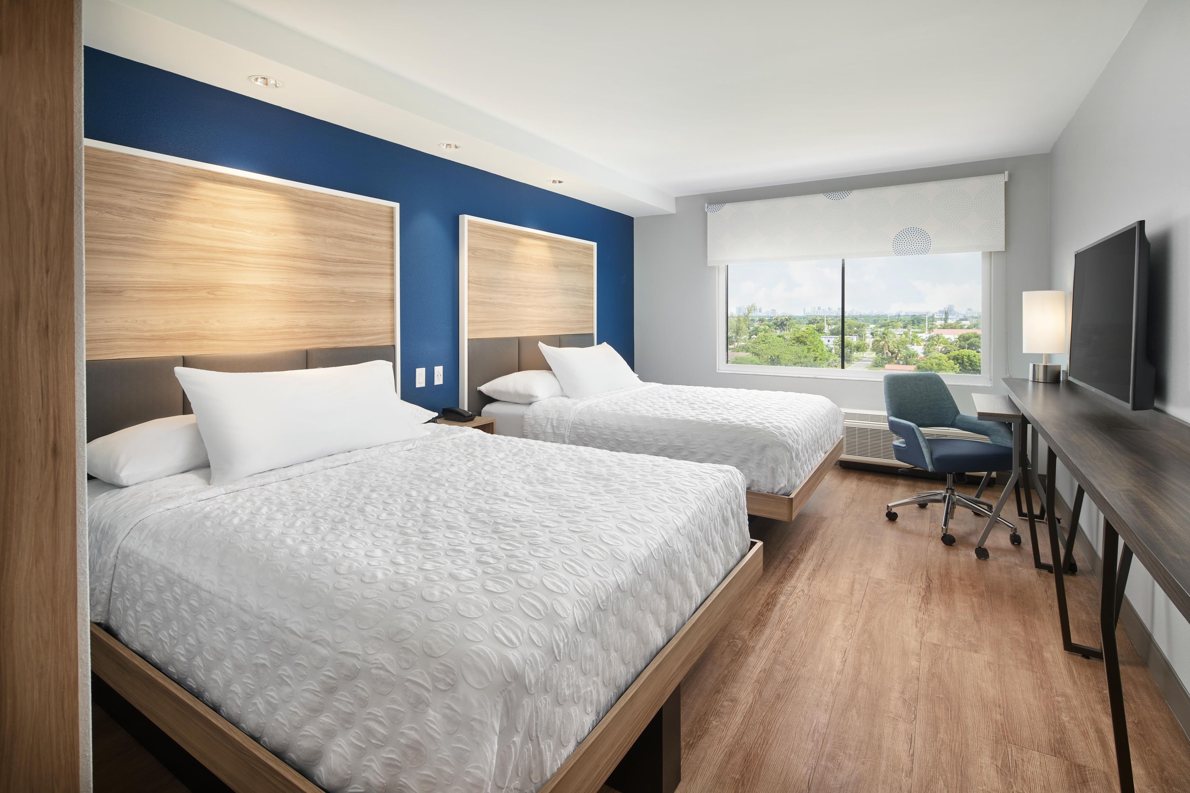 A hotel room with two beds, a desk, a chair, and a television.