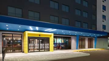 Una entrada de hotel moderna con un toldo azul, puertas de cristal y una pared de acento amarilla.