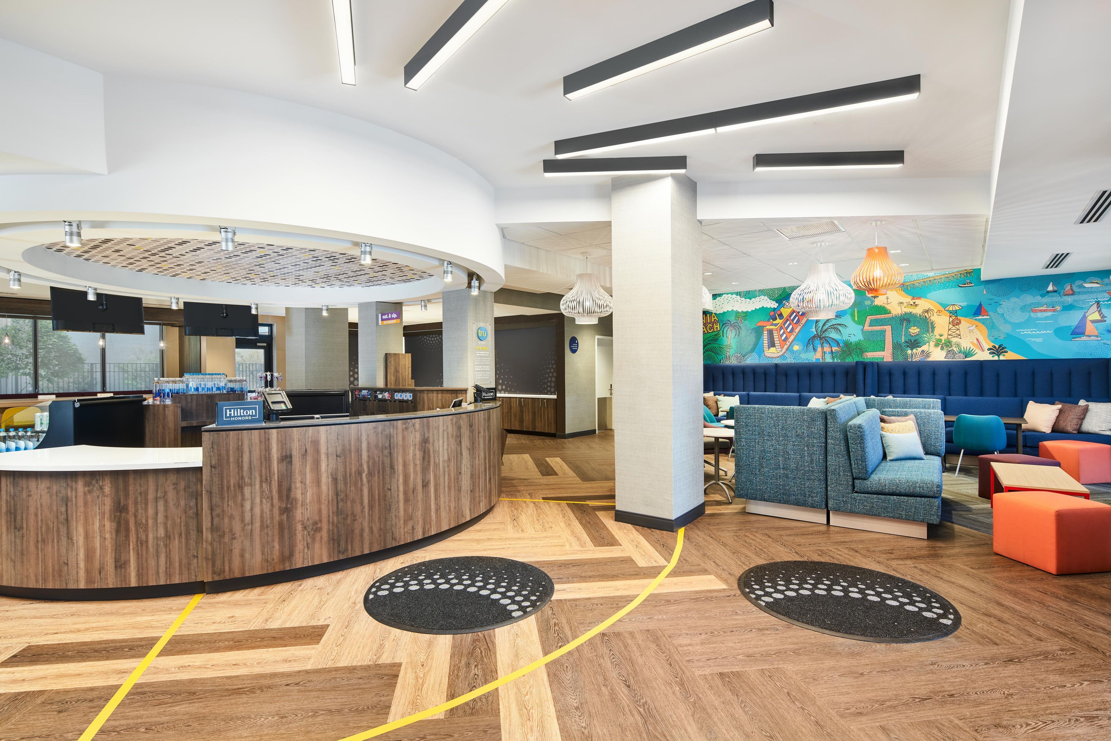 A hotel reception area with a curved desk, a blue seating area with colorful cushions, and a mural depicting a beach scene.