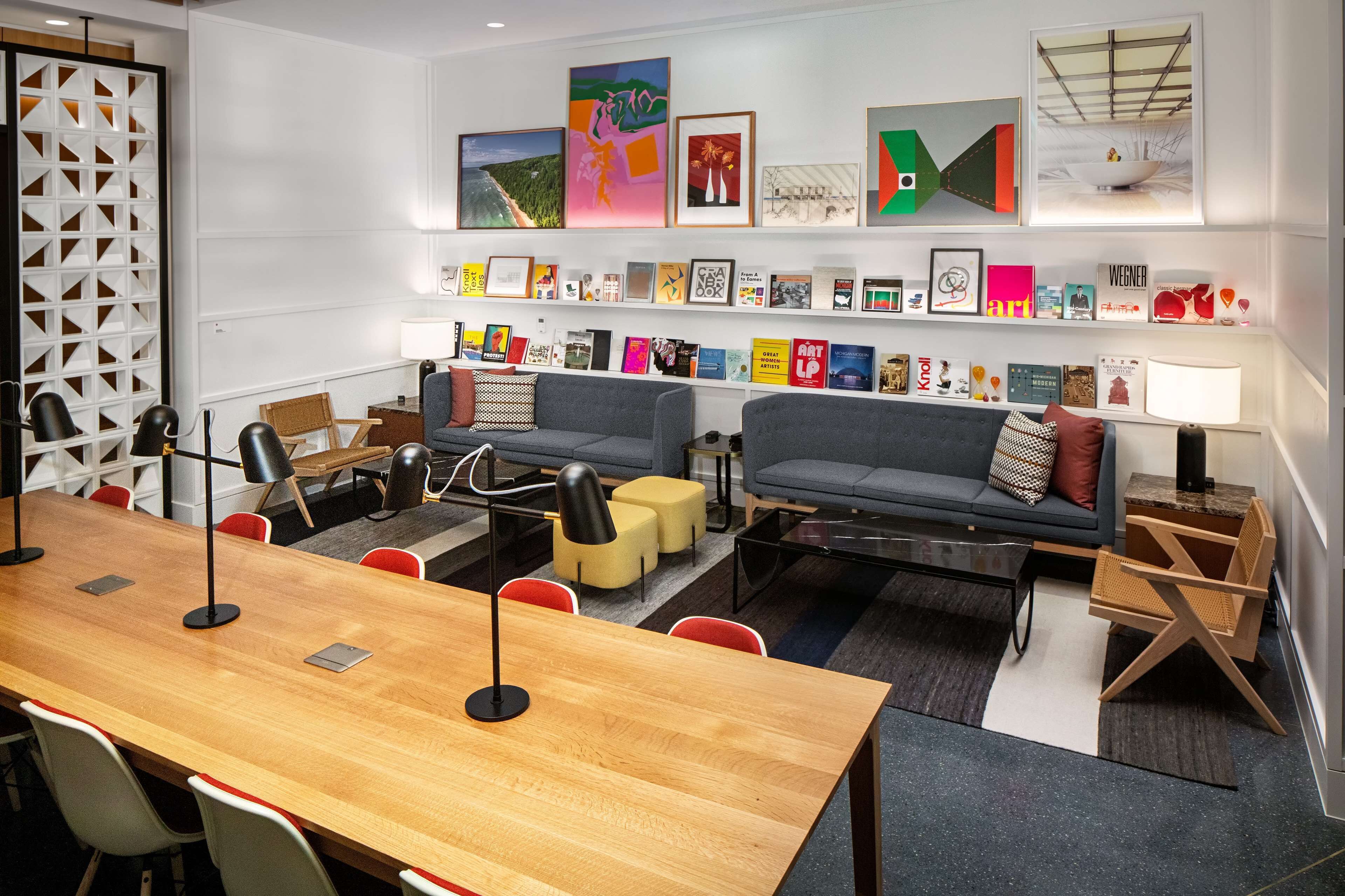 A modern meeting room with a long wooden table, two sofas, and a bookshelf with various books and framed pictures.