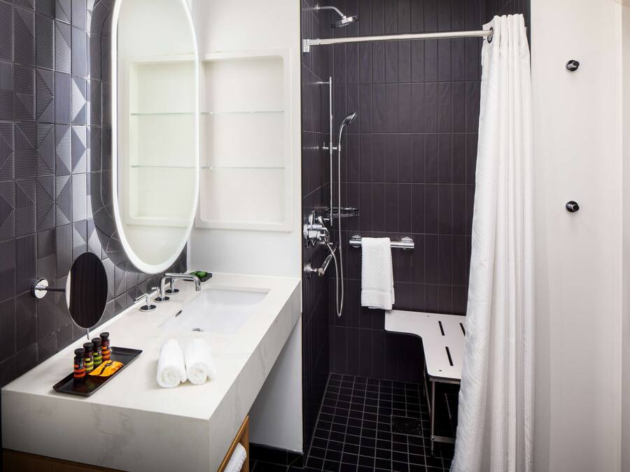 A modern bathroom with a large mirror, white sink, and black tiled walls.