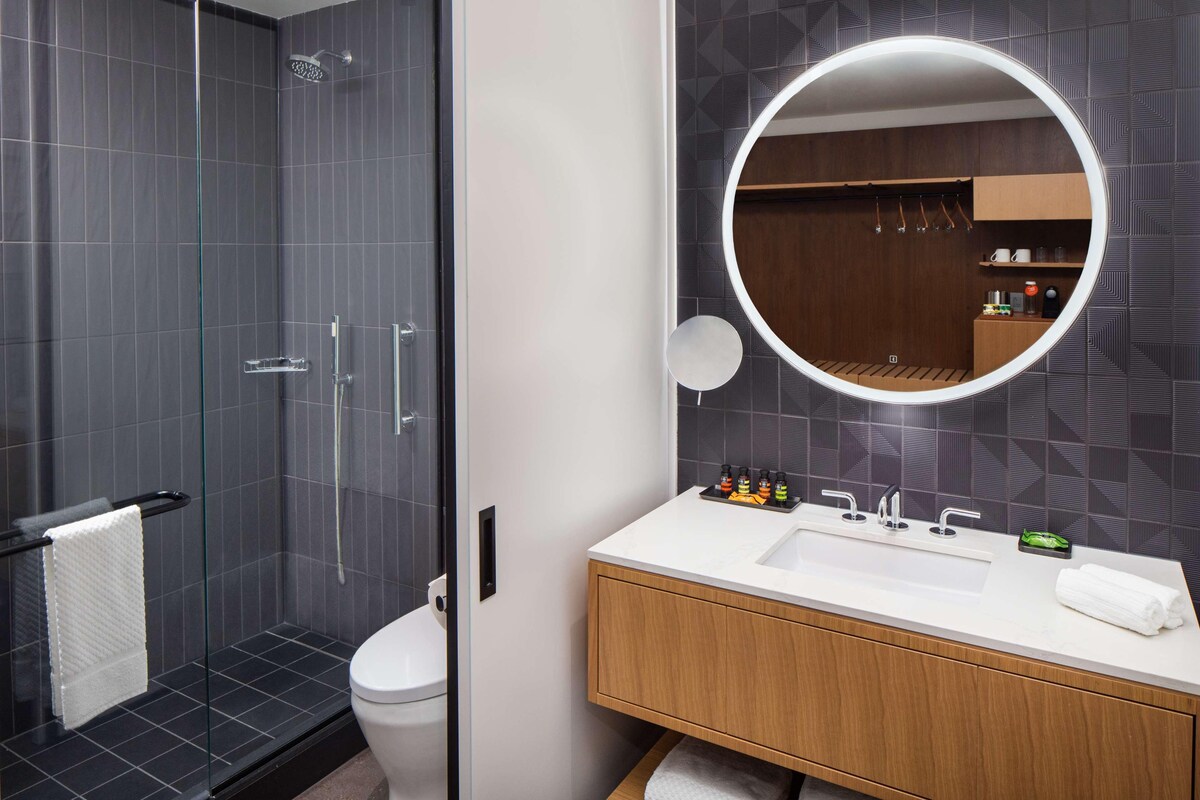 A modern bathroom with a glass shower enclosure, a white toilet, a wooden vanity with a sink, and a large mirror.