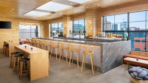 Un espace bar moderne, doté de meubles en bois, d’un comptoir en marbre et de grandes fenêtres offrant une vue sur la ville.