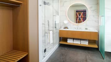 A modern bathroom with a glass-enclosed shower, a wooden vanity, and a marble-tiled wall.