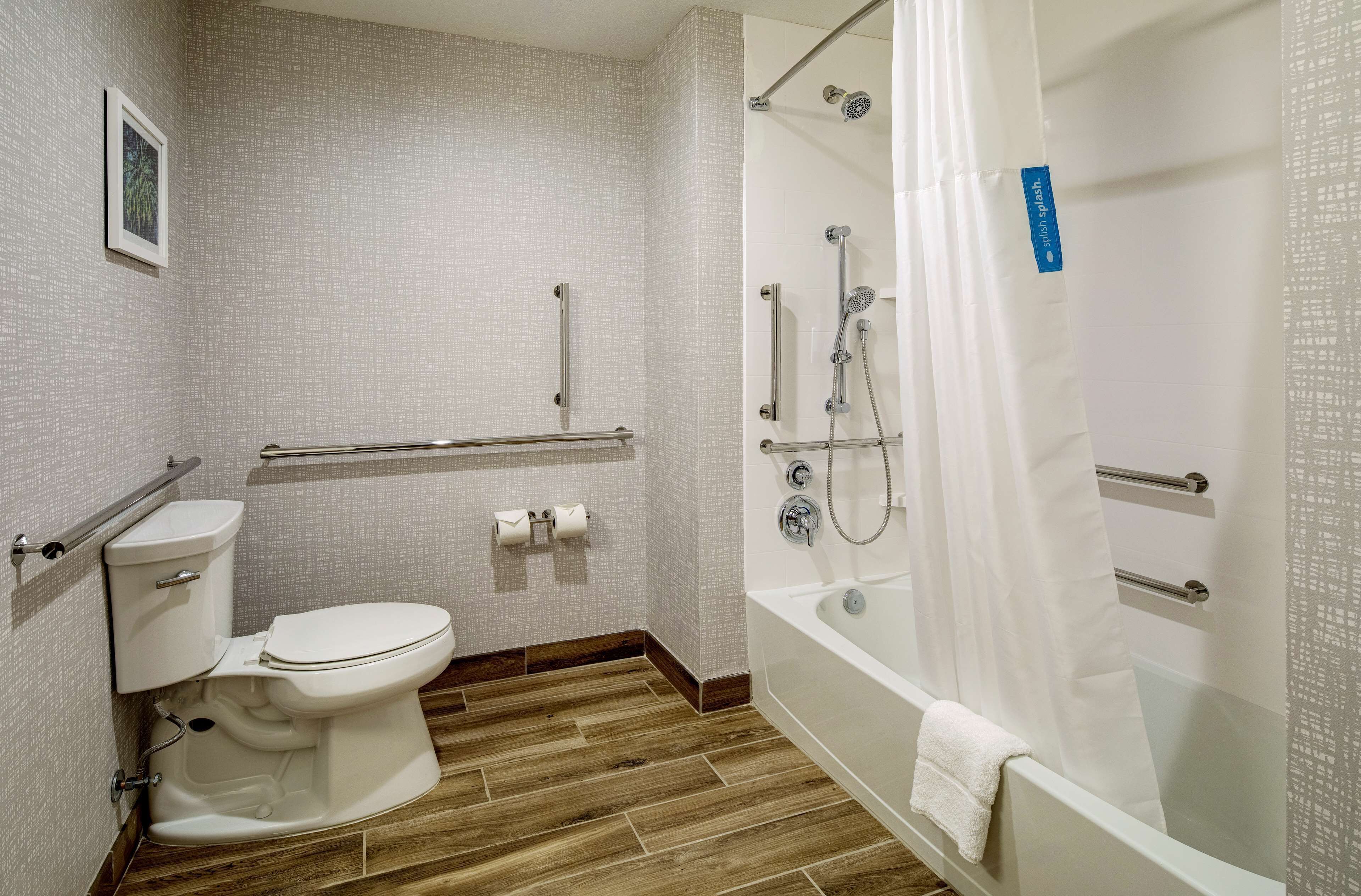 Un baño moderno con inodoro, ducha y barras de apoyo.