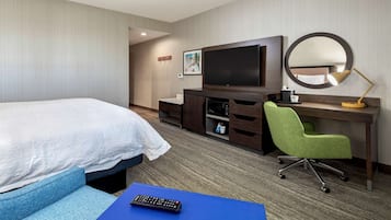 A hotel room with a bed, a desk with a computer, a chair, a TV, and a mirror.