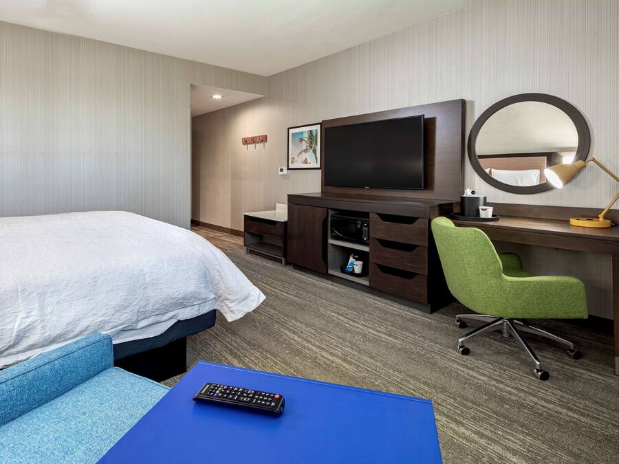 A hotel room with a bed, a desk with a computer, a chair, a TV, and a mirror.
