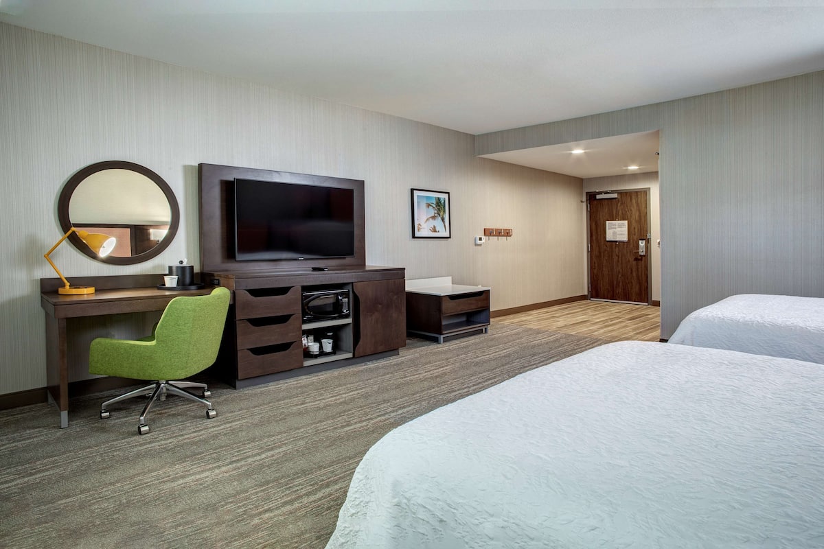 A hotel room with a bed, a desk with a chair, a television, and a small cabinet.