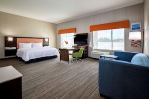 A hotel room with a bed, desk, TV, and seating area.