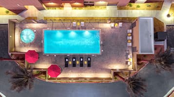 An aerial view of a hotel with a large swimming pool, sun loungers, and a hot tub.
