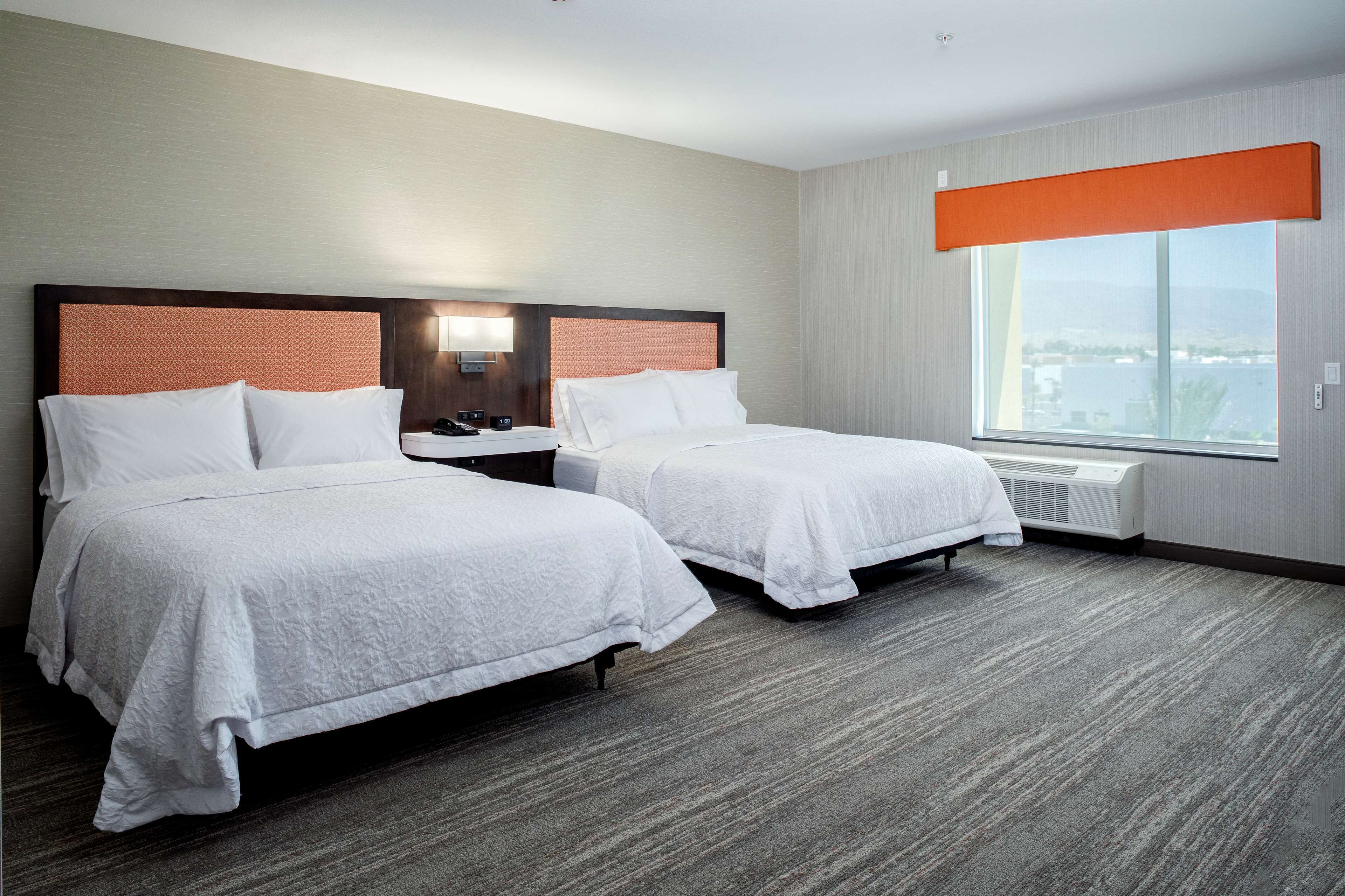 A hotel room with two beds, a large window, and a view of the city.