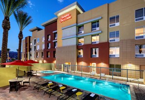 A hotel with a swimming pool, outdoor seating, and palm trees.