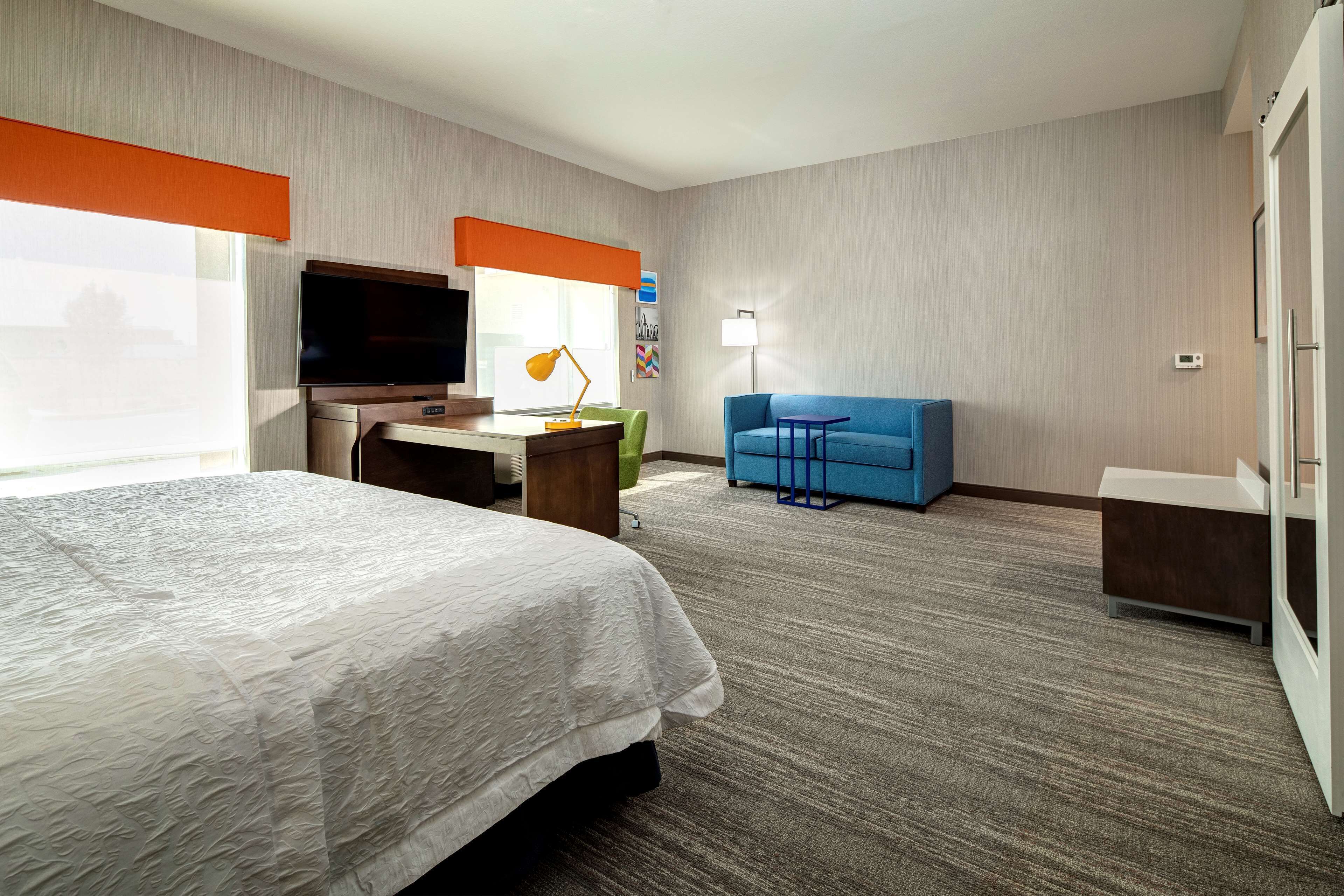 A hotel room with a bed, desk, TV, and a blue sofa.