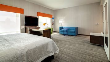 A hotel room with a bed, desk, TV, and a blue sofa.