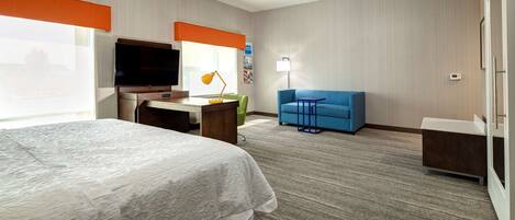 A hotel room with a bed, desk, TV, and a blue sofa.