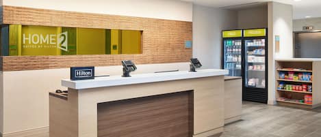 A hotel reception area with a reception desk, a digital display, and a self-service beverage station.