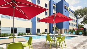 A hotel pool area with red umbrellas, green chairs, and a pool table. - Home2 Suites by Hilton Palm Bay Melbourne I 95 (Palm Bay)