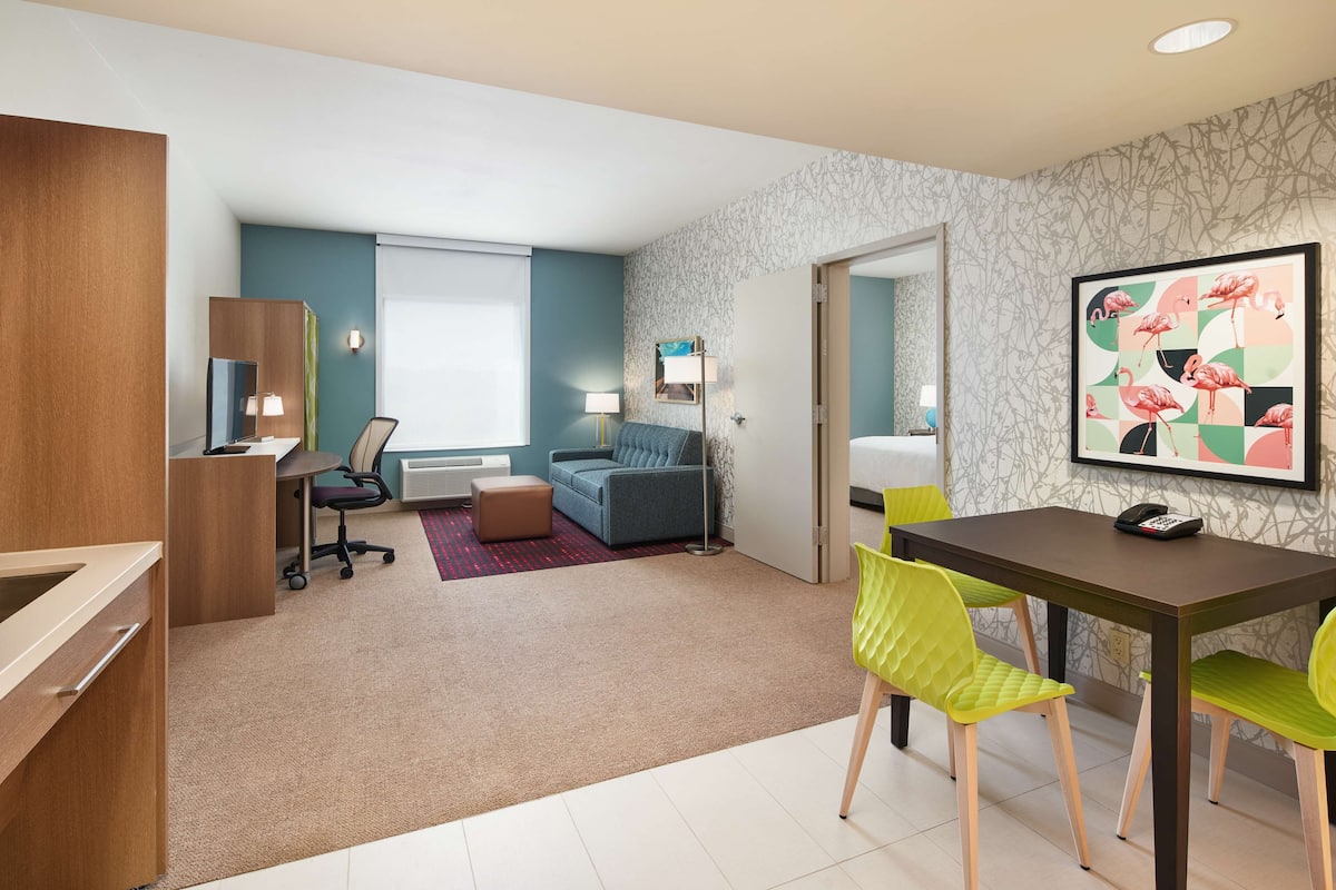 Une chambre d’hôtel moderne comprenant un coin repas, un canapé, un bureau et un grand tableau au mur.