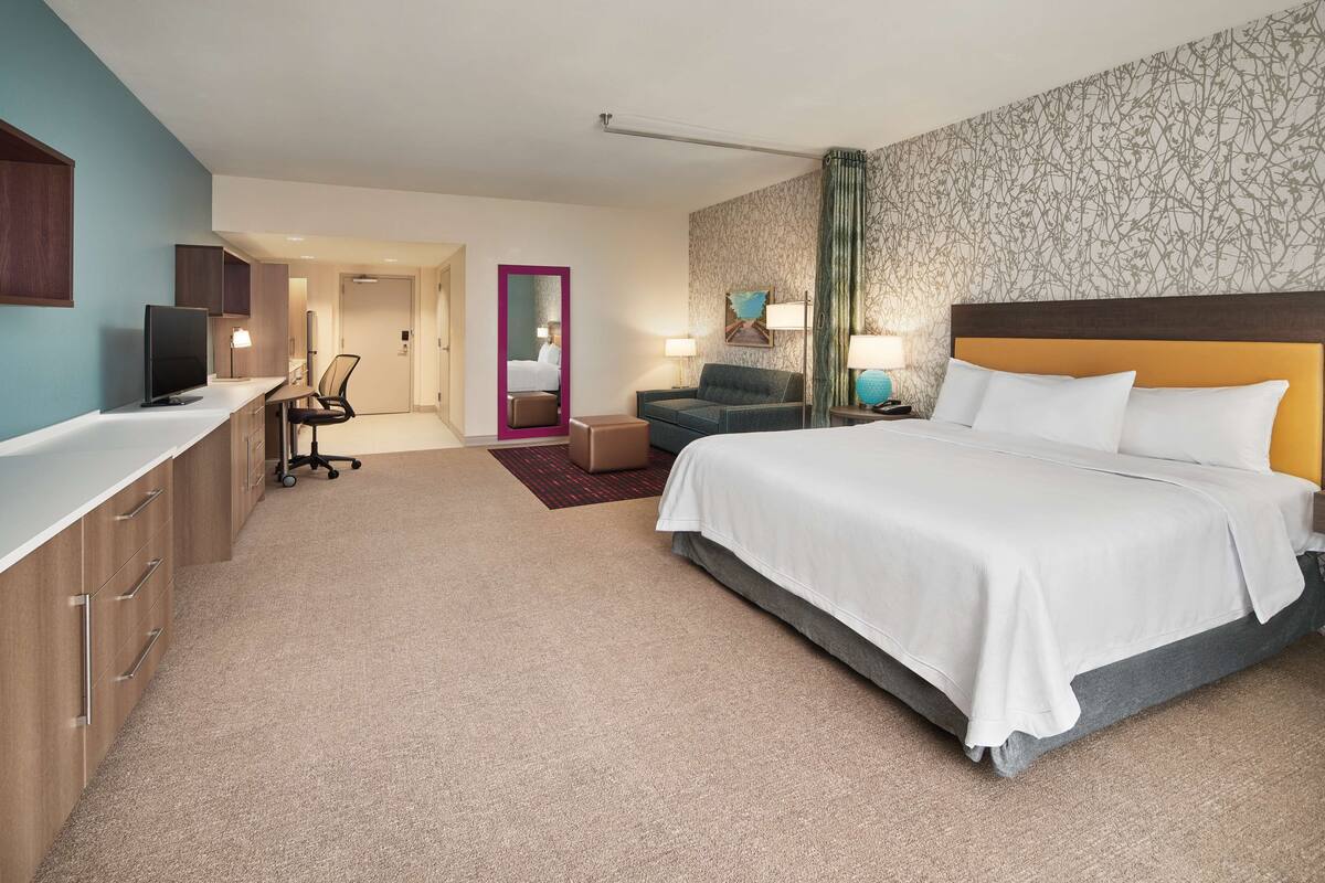 Une chambre d’hôtel avec un lit, un bureau, une chaise et un miroir.