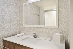 Un baño con lavamanos blanco, un espejo y un papel tapiz estampado.