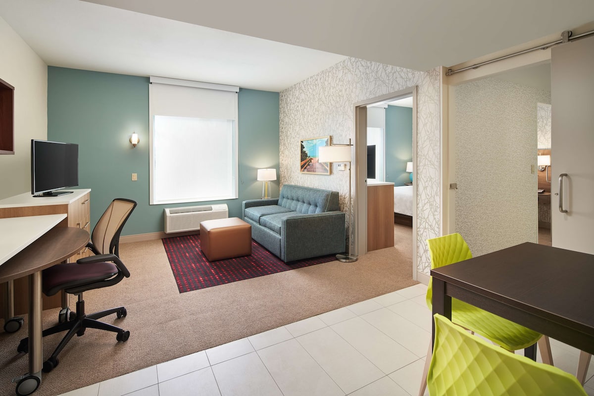 Une chambre d’hôtel moderne équipée d’un bureau, d’un fauteuil de bureau, d’un canapé et d’un coin repas avec des chaises.