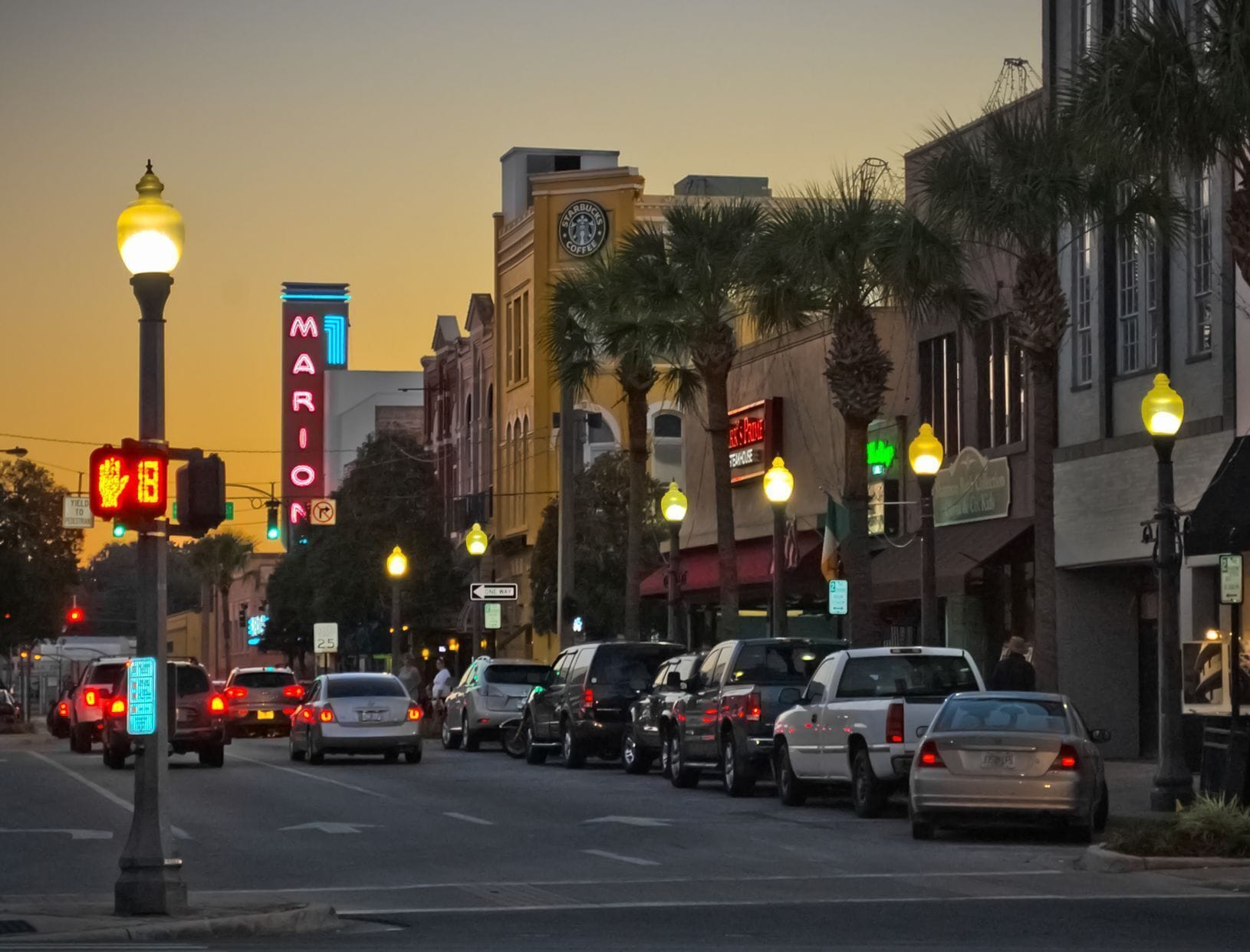 Una calle flanqueada por vehículos estacionados y farolas iluminadas.