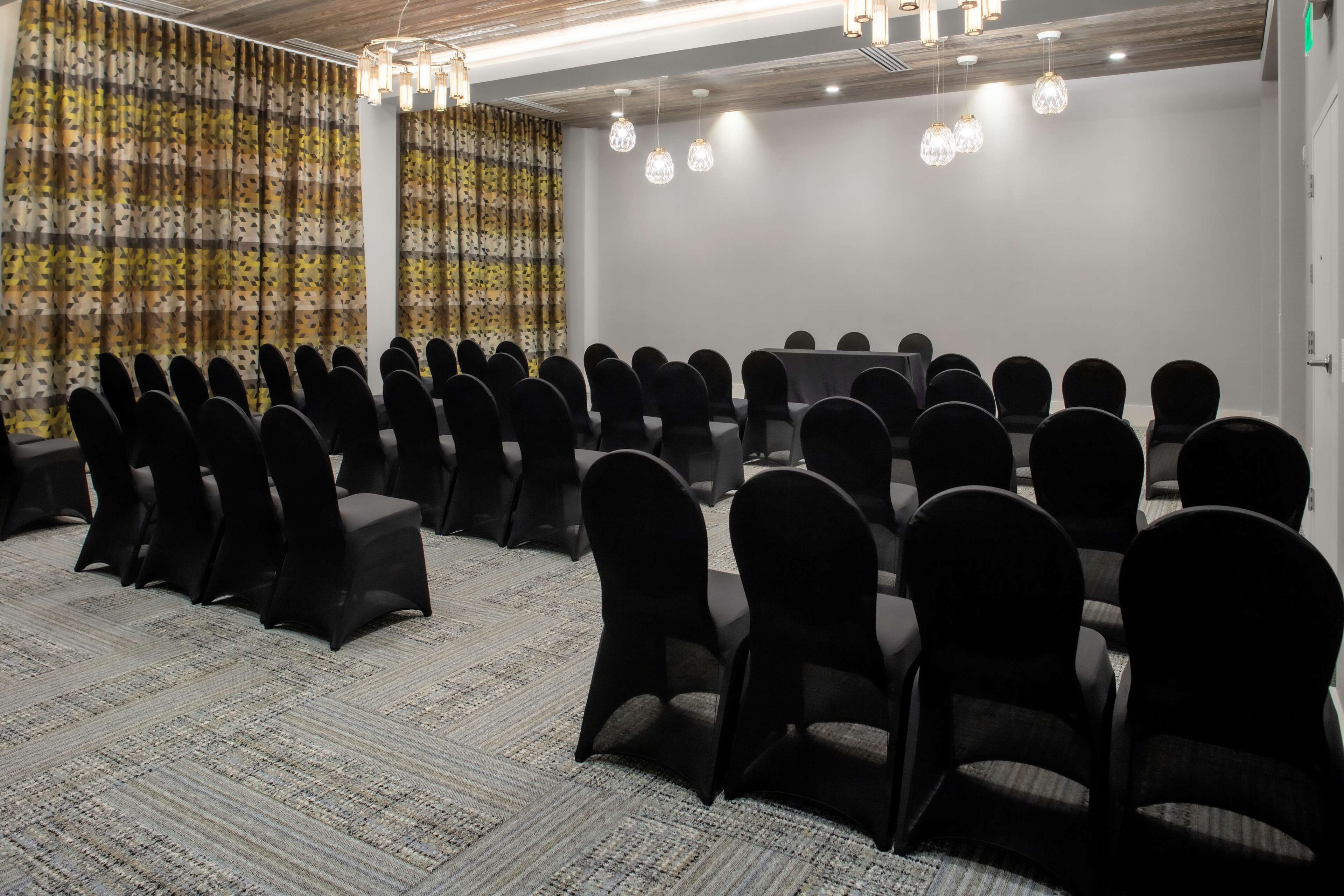 A conference room with rows of chairs, a long table, and decorative curtains.