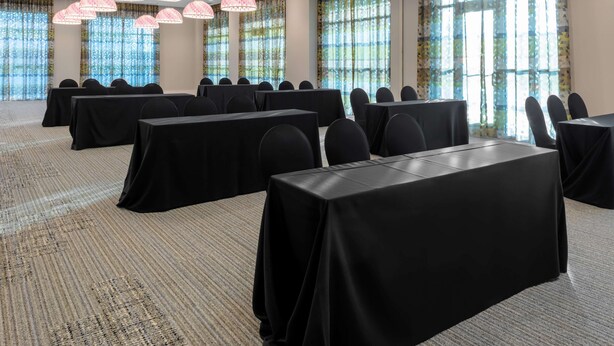 A conference room with tables and chairs, large windows with curtains, and hanging lamps. - Hilton Garden Inn Ocala Downtown (Ocala)