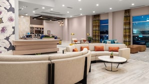 A modern hotel lobby with a curved seating area, a reception desk, and large windows offering city views. - Hilton Garden Inn Ocala Downtown (Ocala)