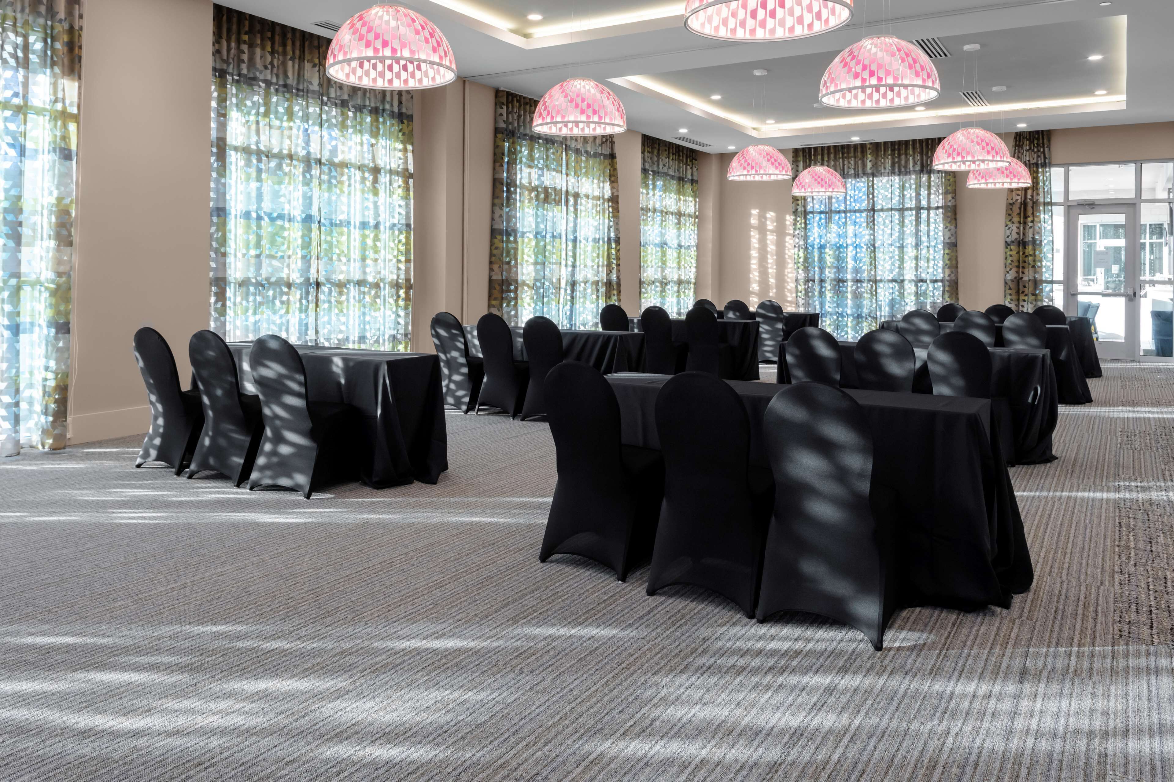 A conference room with rows of tables and chairs, large windows with curtains, and decorative ceiling lights.