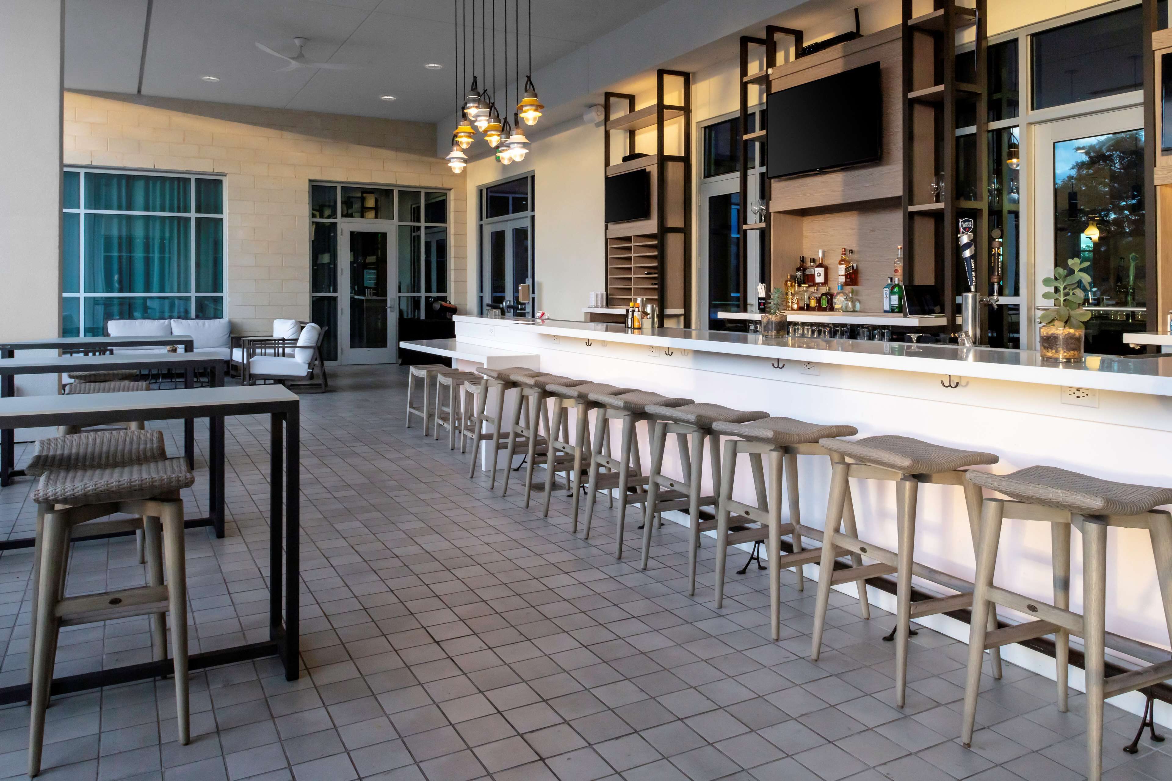 A modern bar area with a long counter, multiple stools, and a television mounted on the wall.