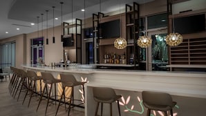 A modern bar area with a long counter, multiple stools, and hanging pendant lights. - Hilton Garden Inn Ocala Downtown (Ocala)