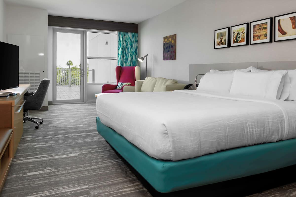 A hotel room with a large bed, a desk with a computer, a chair, and a TV.