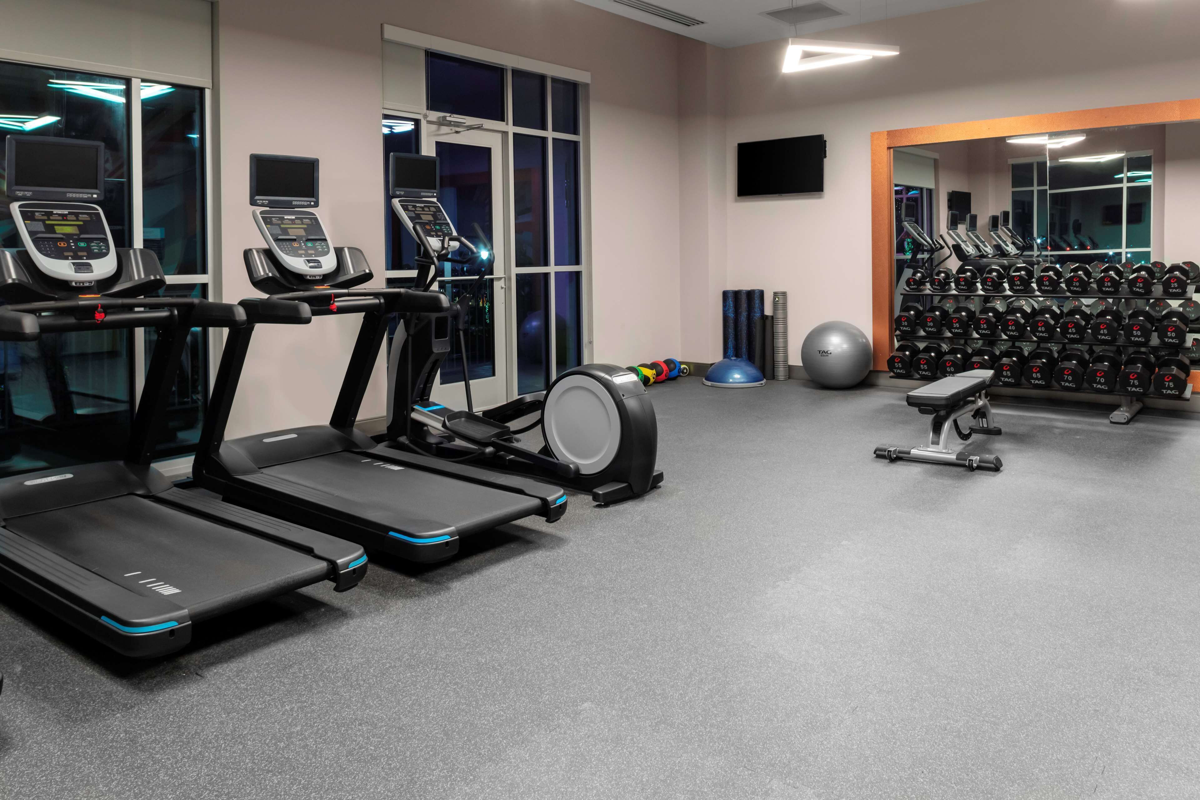 A gym with treadmills, an elliptical, a set of dumbbells, and exercise balls.