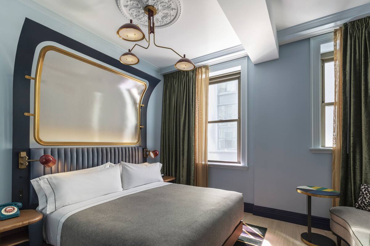 A hotel room with a large bed, a round table, a small desk, and a window with curtains.