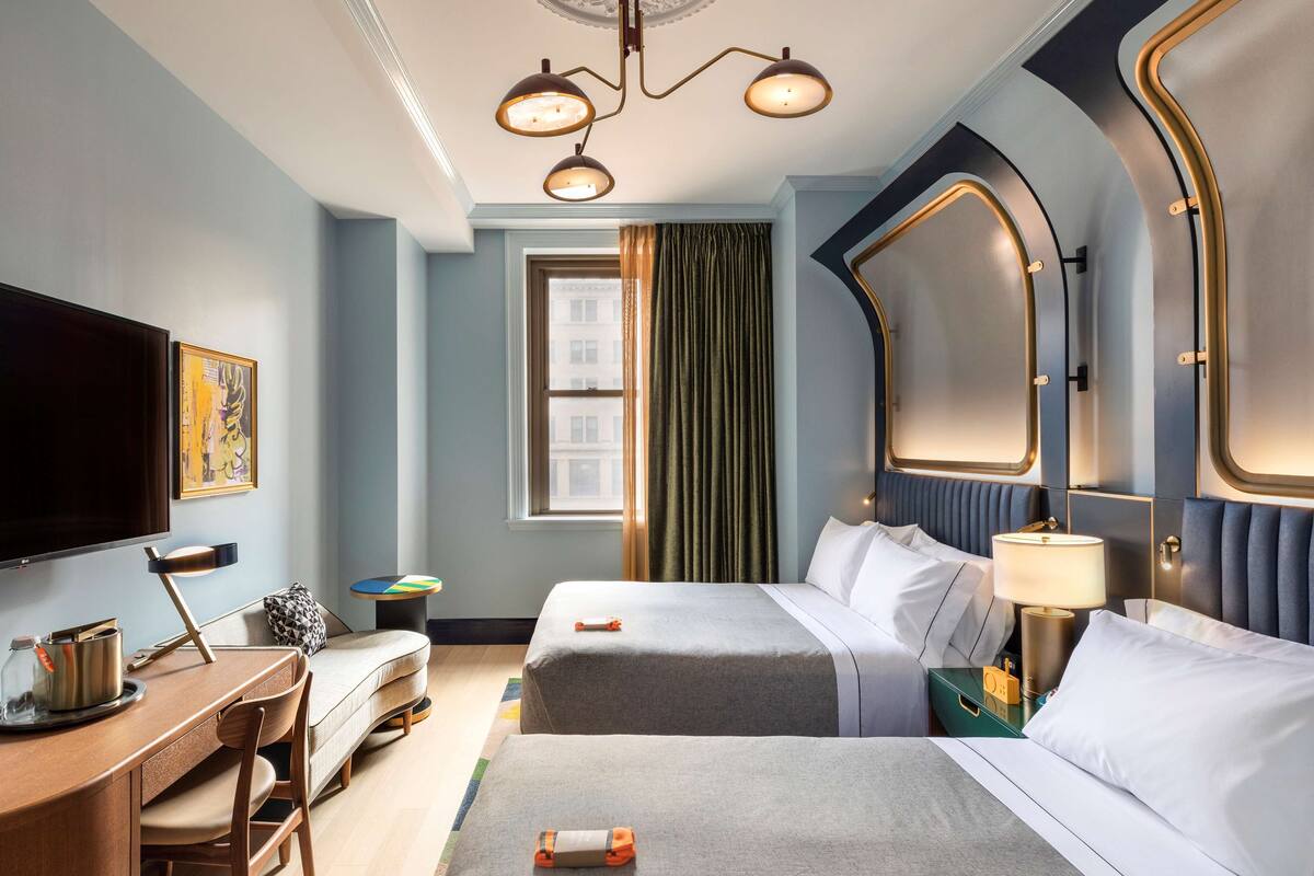 A hotel room with two beds, a desk with a chair, a television, and a window with curtains.