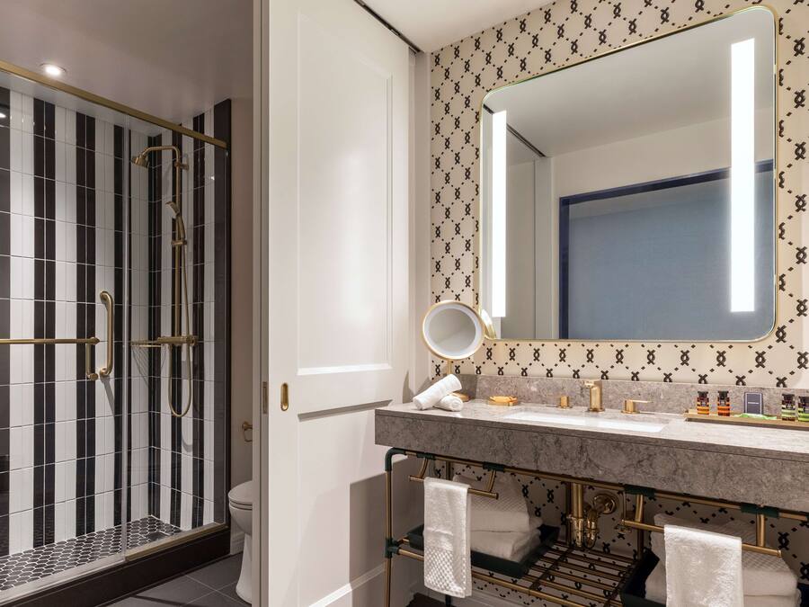 Un baño moderno con ducha de vidrio, tocador de mármol y un espejo grande con marco dorado.