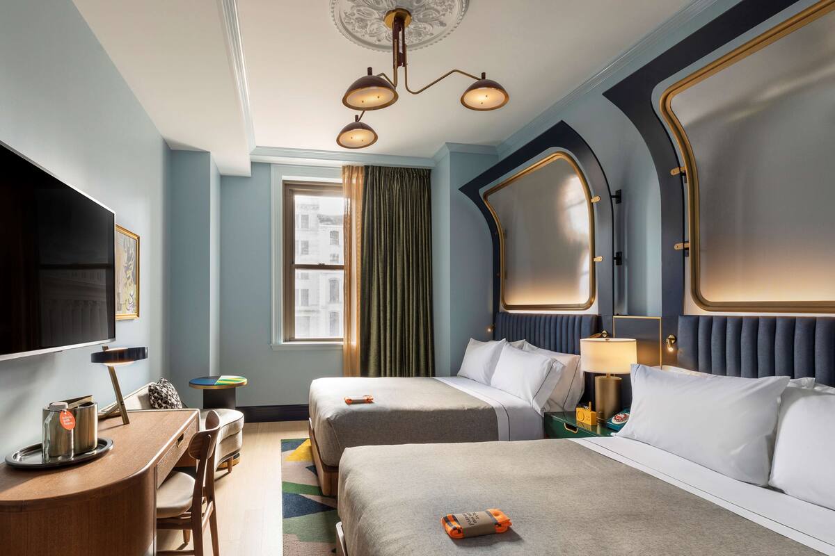 A hotel room with two beds, a desk, a TV, and a window with curtains.