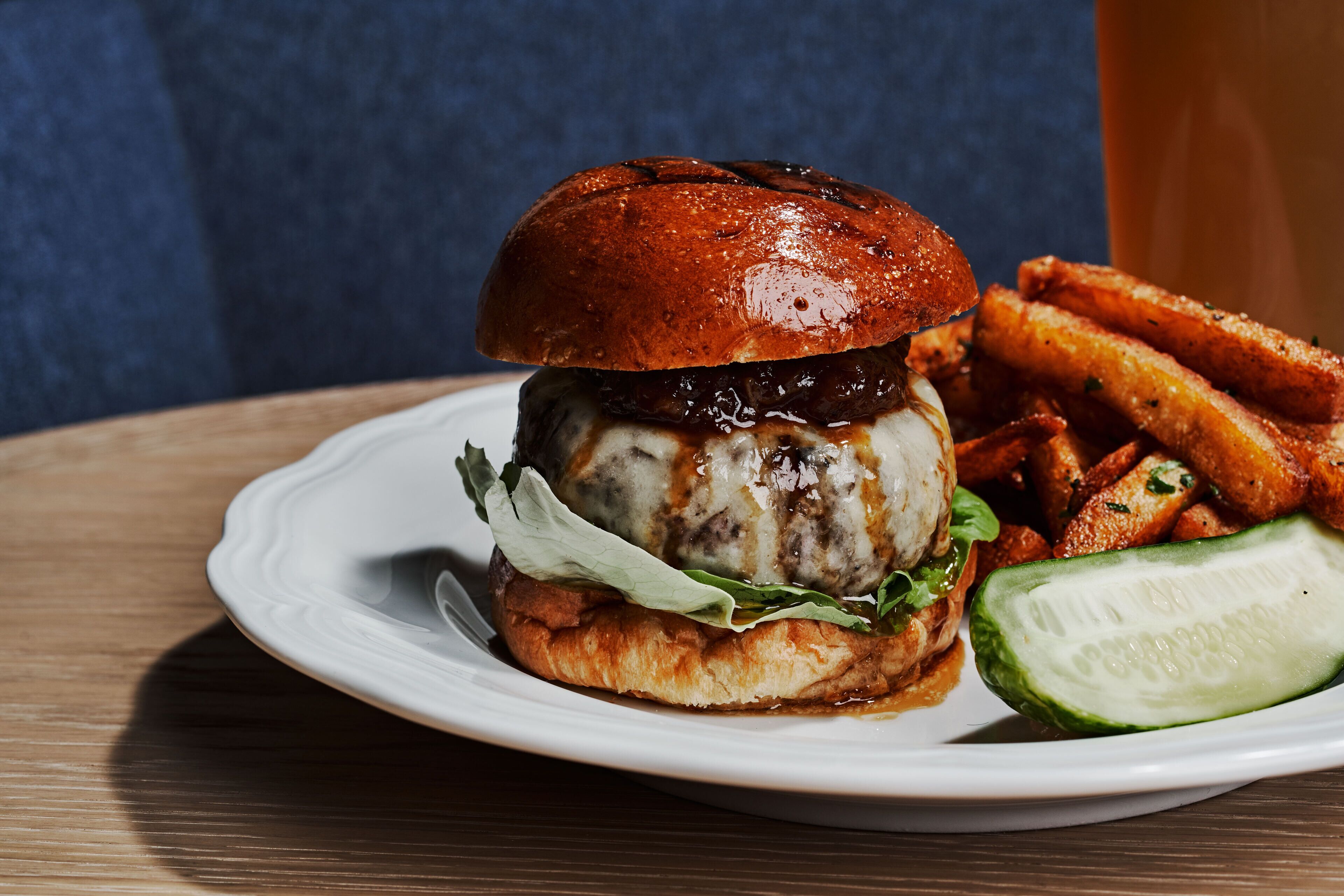 A burger with fries and a slice of cucumber on a white plate.