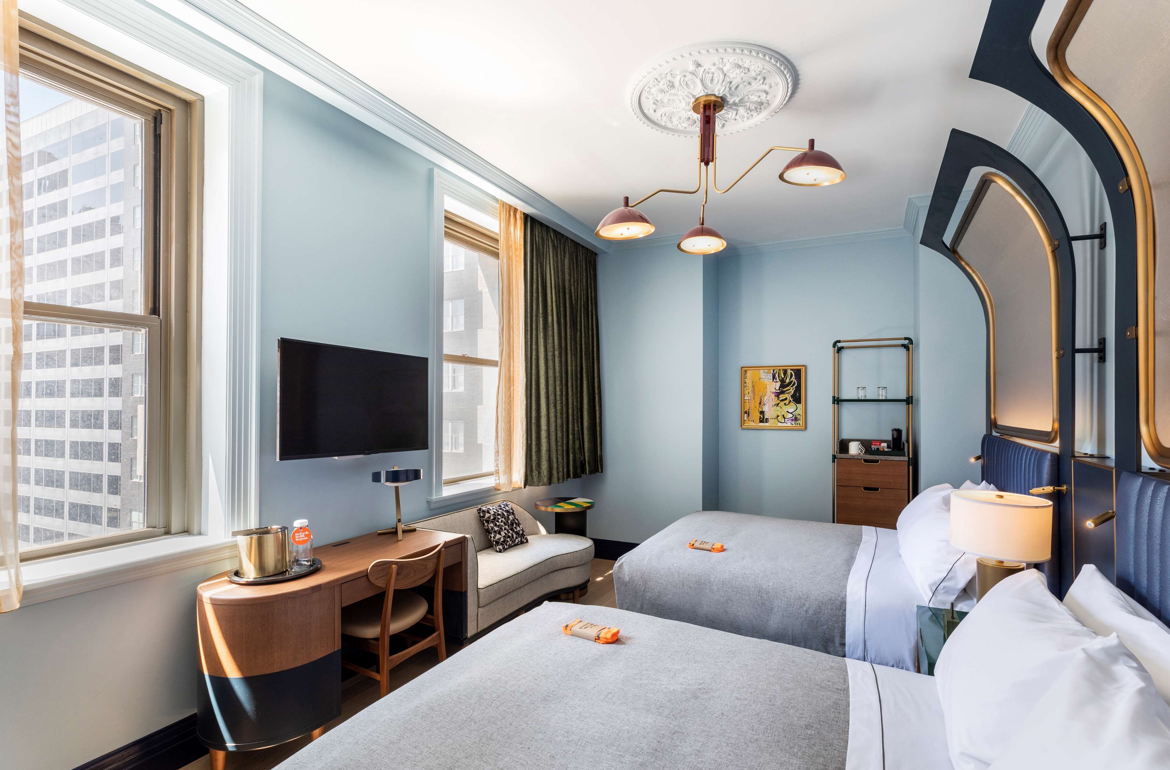 Habitación de hotel con dos camas, un escritorio, un televisor, un espejo y una ventana con vistas a la ciudad.