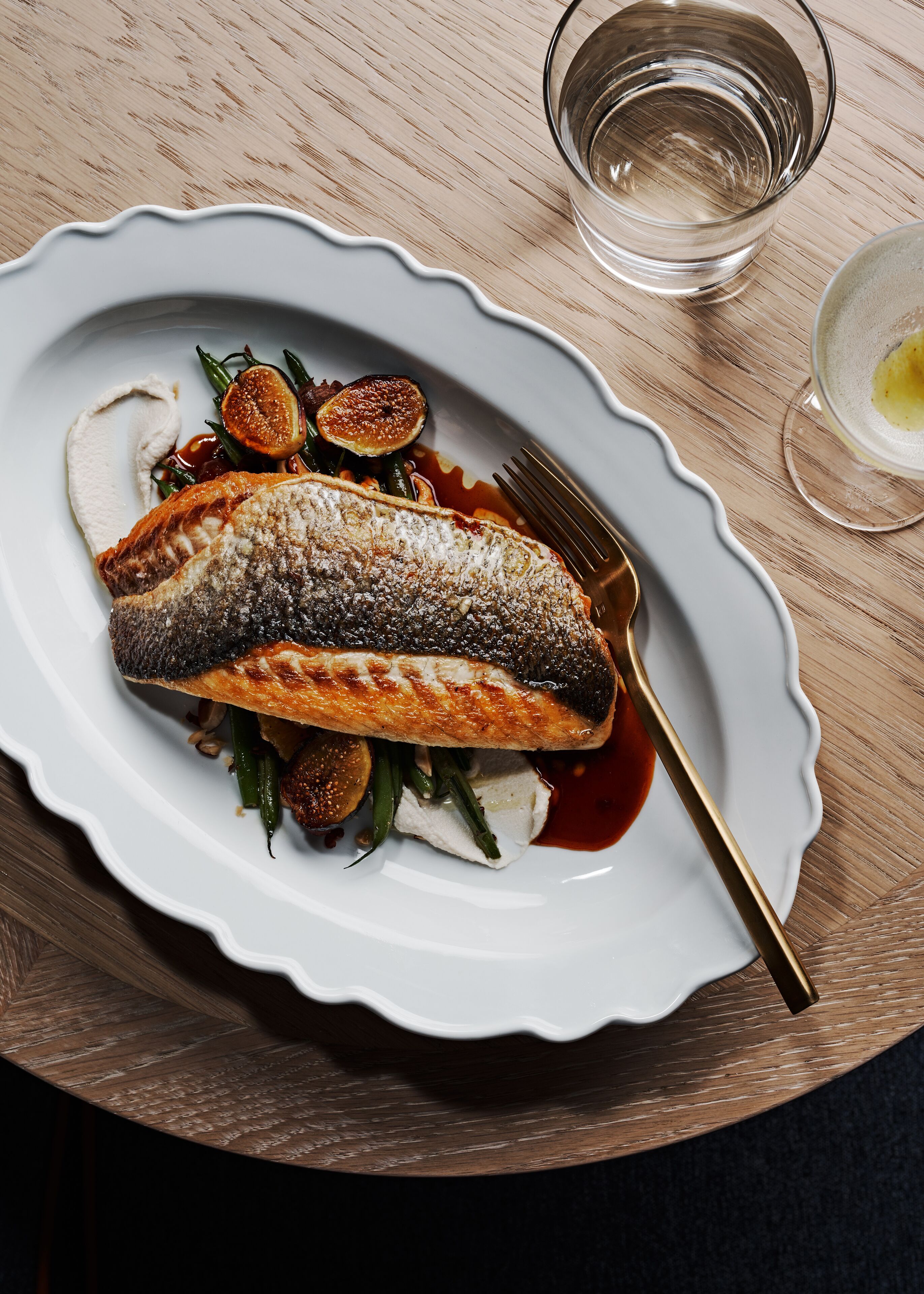 Une assiette blanche contenant du poisson, des légumes et de la sauce, posée sur une table en bois.