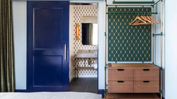 A hotel room with a blue door, a wooden dresser, and a hanging rack with clothes.