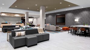 A modern living area with a sectional sofa, a dining table with chairs, and a kitchen in the background. - Hilton Garden Inn Chandler Downtown (Chandler)