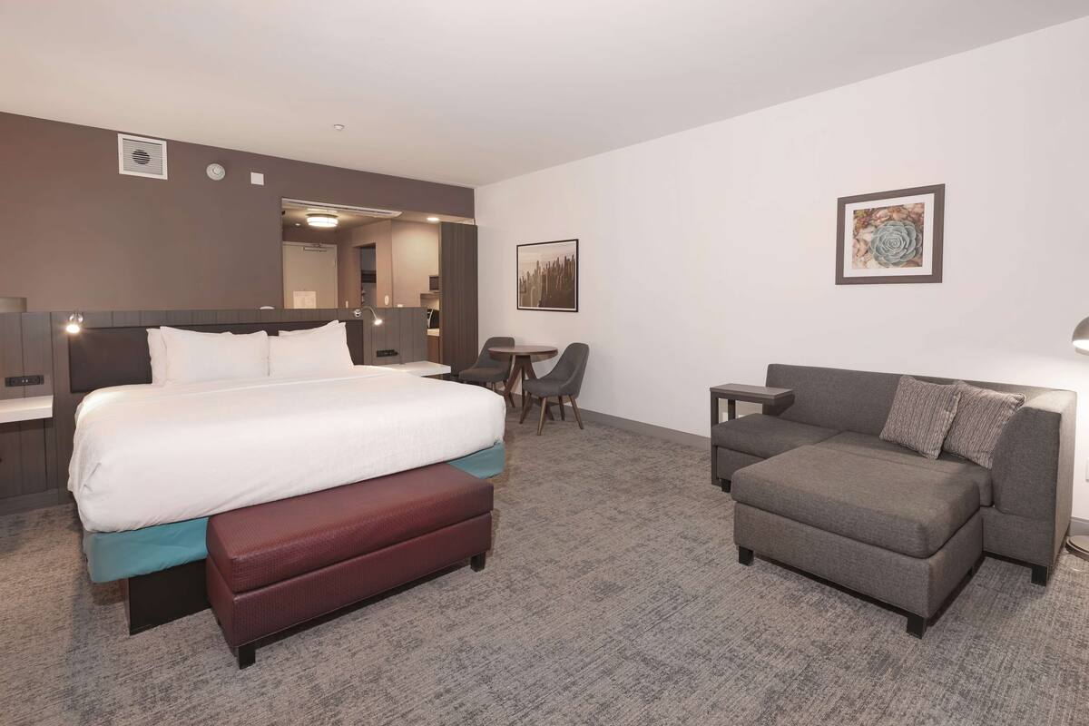 A hotel room with a bed, a sofa, a small table, and a chair.