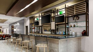 A modern bar area with a long counter, multiple TV screens, and a variety of bottles and glasses. - Hilton Garden Inn Chandler Downtown (Chandler)