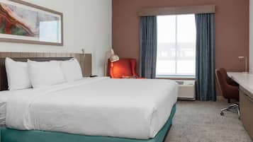 Una habitación de hotel con una cama grande, un escritorio, una silla naranja y una ventana con cortinas.
