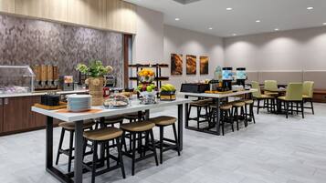 A modern hotel kitchen with a central island, bar stools, and a seating area with chairs.